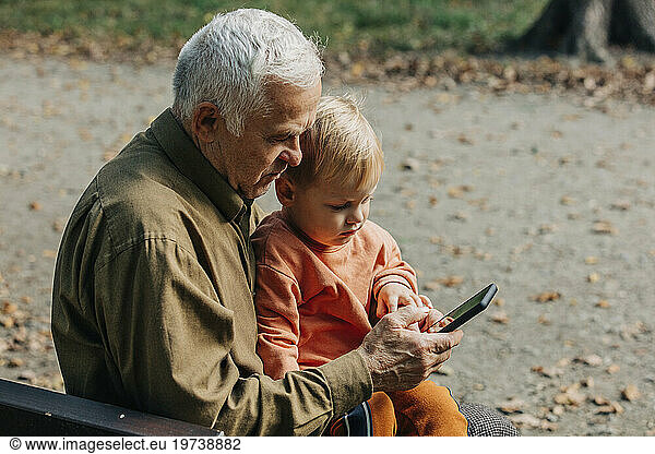 Grandfather showing smart phone to grandson at park
