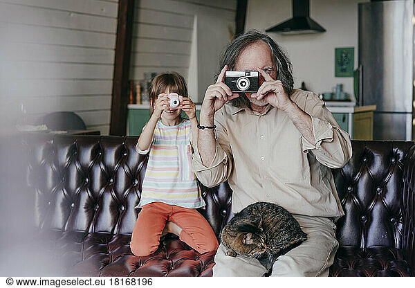 Grandfather with vintage camera and granddaughter with toy camera taking photos at home