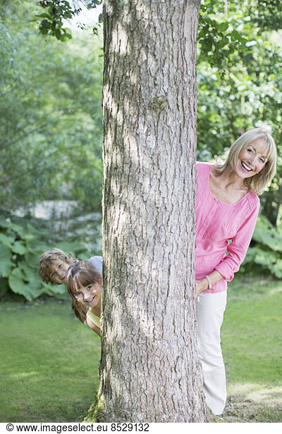 Grandmother and grandchildren peering behind tree
