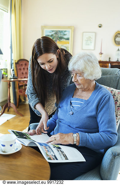 Grandmother and granddaughter reading magazine together in living room