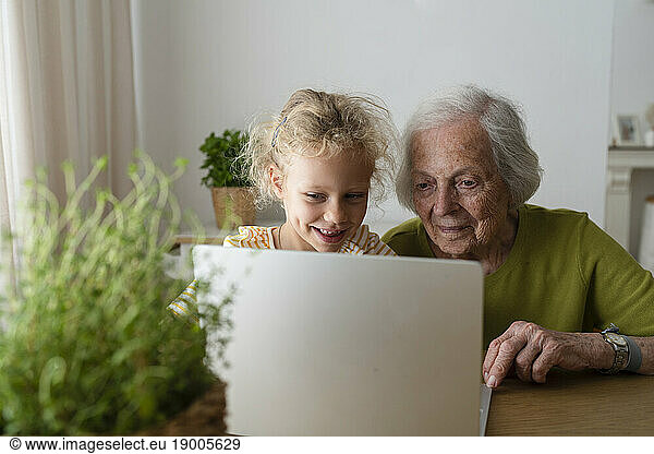 Grandmother and granddaughter using laptop on table