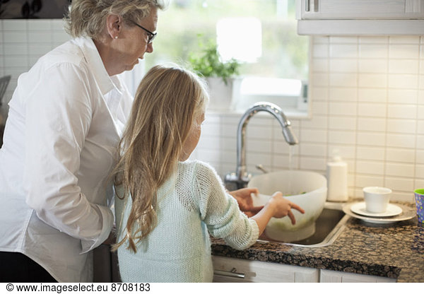 Grandmother and granddaughter washing vegetables in kitchen
