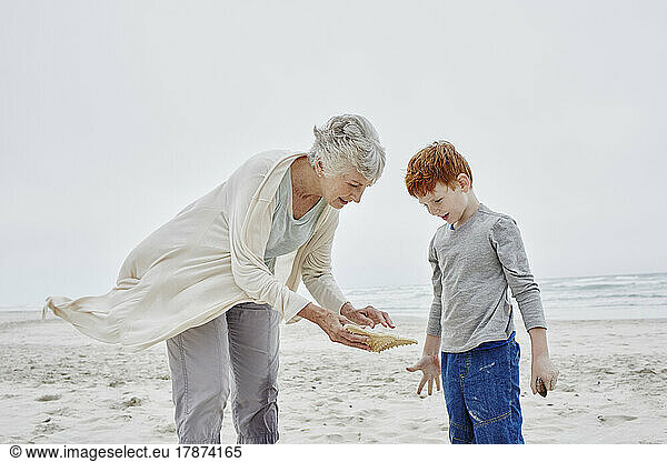 Grandmother and grandson standing on beach looking at seashell
