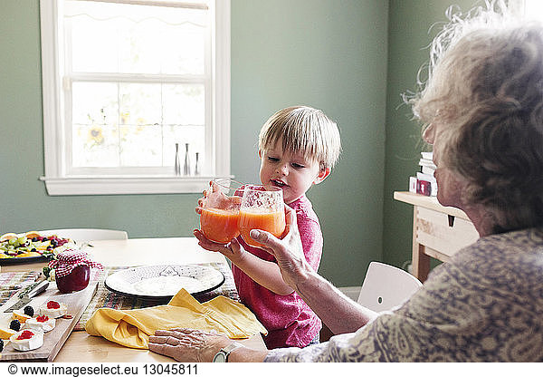 Grandmother and grandson toasting juice at dining table