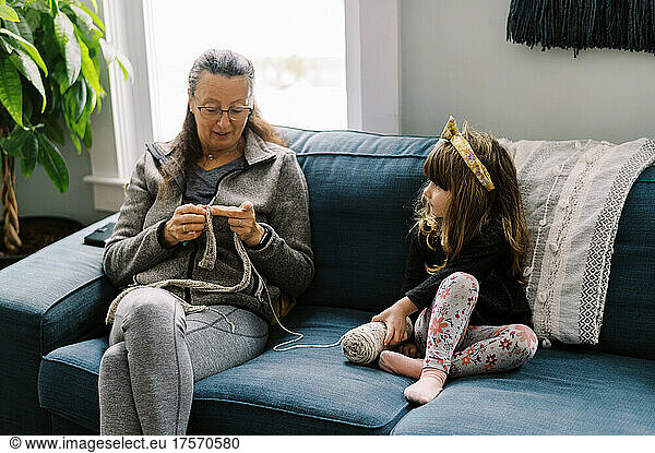Grandmother and her granddaughter on the couch crocheting