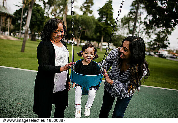 Grandmother and mother pushing little girl laughing in swing