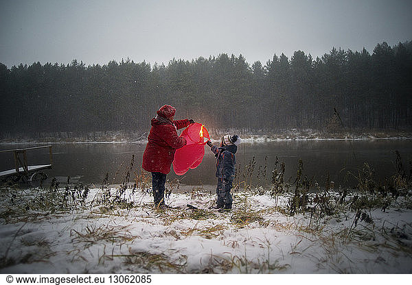 Grandmother and son holding paper lantern on snow covered field