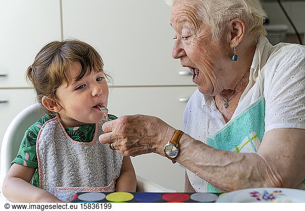Grandmother feeding granddaughter in the kitchen