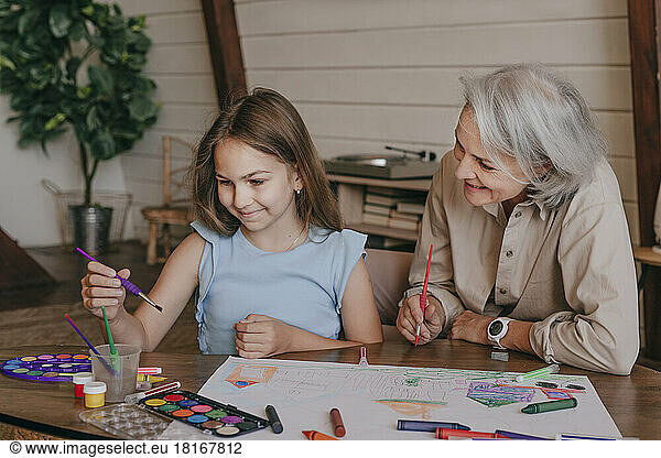 Grandmother helping granddaughter in painting at home