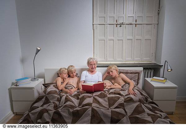 Grandmother in bed with grandsons reading story book
