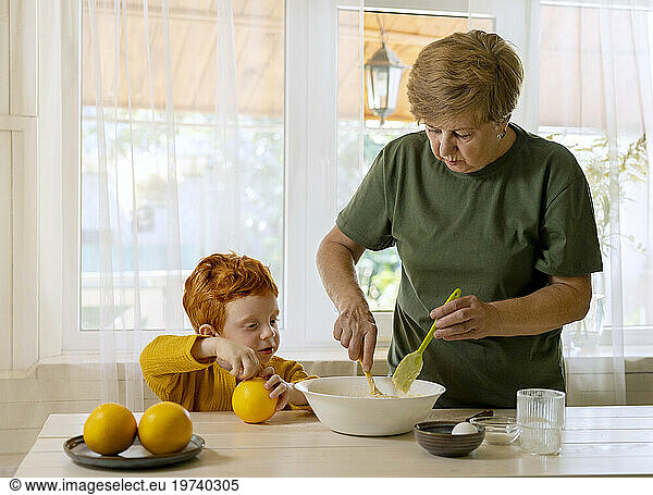 Grandmother mixing batter in bowl with grandson at table