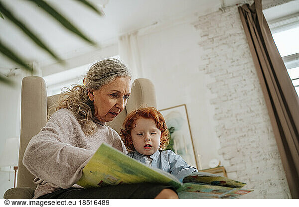Grandmother reading book with grandson at home