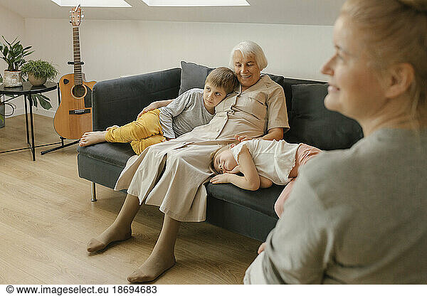 Grandmother sitting with grandchildren on sofa at home