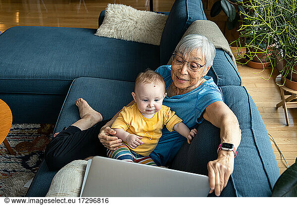 Grandparent sitting with granddaughter using laptop to video call