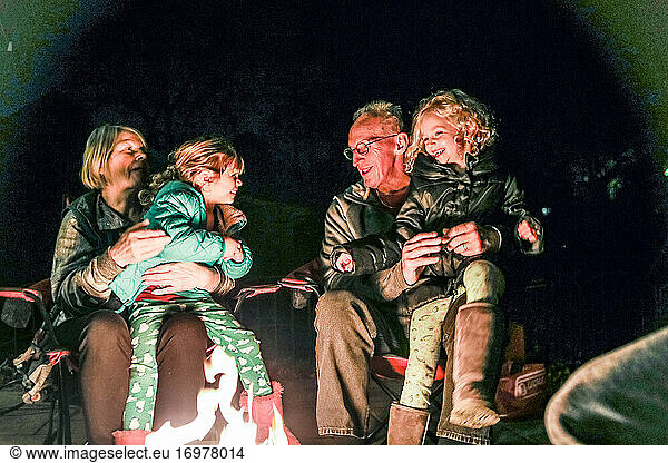 grandparents and grandchildren sitting around fire pit laughing