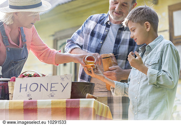 Grandparents and grandson tasting and selling honey at farmer’s market stall