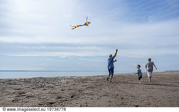 Grandparents flying kite with grandson at beach
