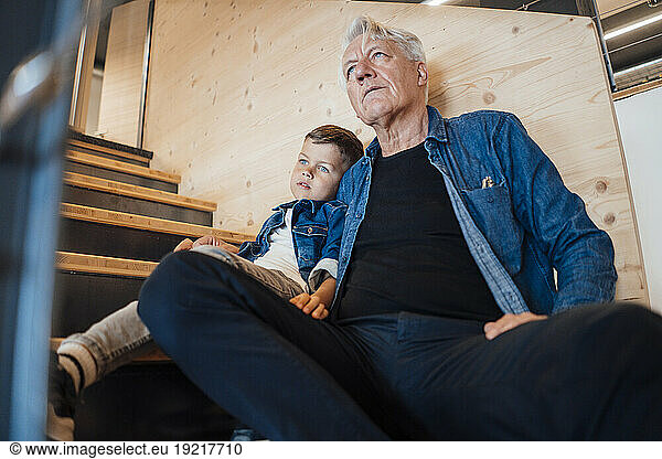 Grandson and grandfather sitting on staircase at home