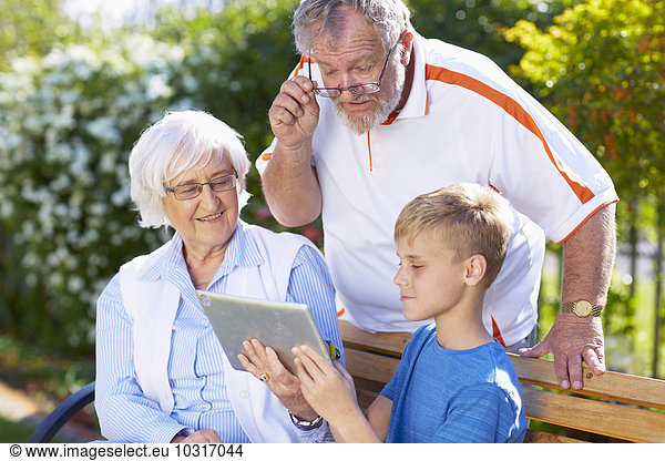 Grandson and grandparents using digital tablet in park