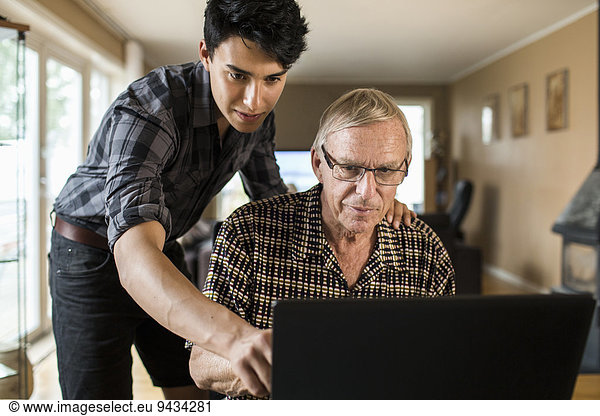 Grandson assisting grandfather in using laptop at home