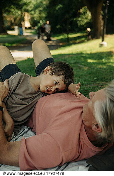 Grandson talking to grandfather lying down at park