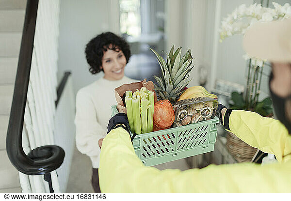 Grateful woman receiving grocery delivery from courier at home