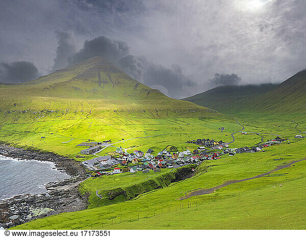 Green landscape and village by sea against cloudy sky  Iceland