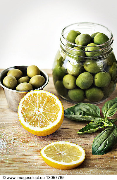 Green olives in containers by sliced lemon on cutting board