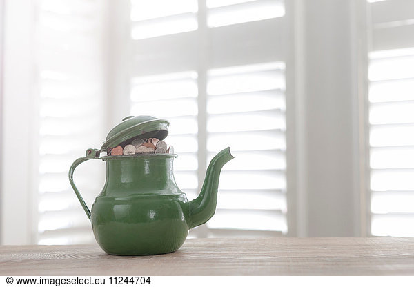 Green vintage teapot full of British coins on table
