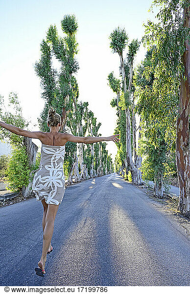 Griechenland  Dodekanes  Kolymbia  Erwachsene Frau hüpft fröhlich entlang einer Eukalyptusallee im Sommer