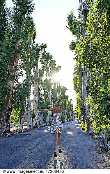 Griechenland  Dodekanes  Kolymbia  Erwachsene Frau hüpft fröhlich entlang einer Eukalyptusallee im Sommer