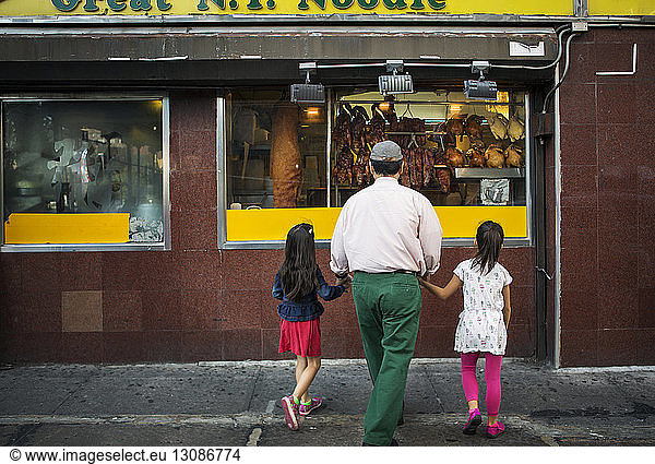 Großvater und Enkelkinder in voller Länge beim Anblick eines Restaurants in der Stadt