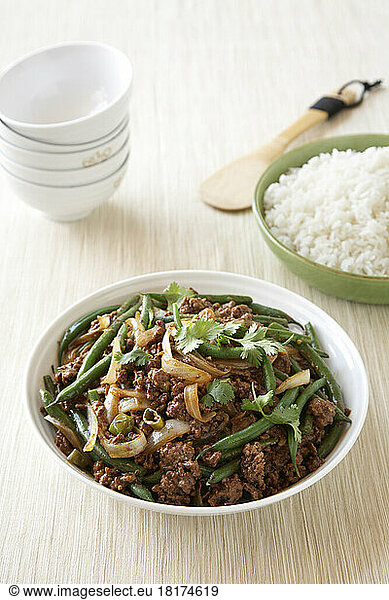 Ground beef stir fry with green beans and onions in white bowl with side dish of rice