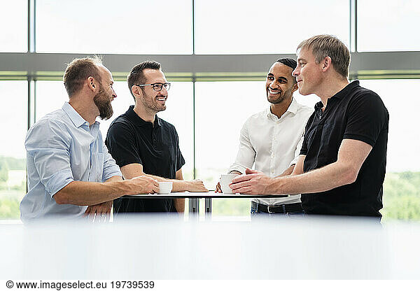 Group of businessman having informal meeting standing in office hall with cups of coffee