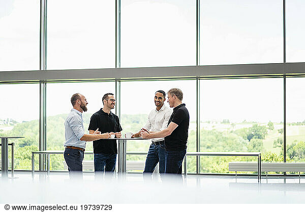 Group of businessman having informal meeting standing in office hall with cups of coffee