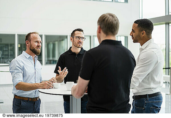 Group of businessman having informal meeting standing in office hall with cups of coffee