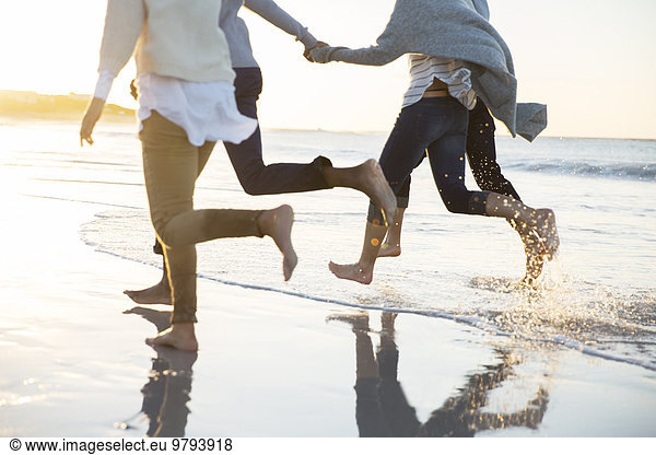 Group of four friends holding hands and running on beach