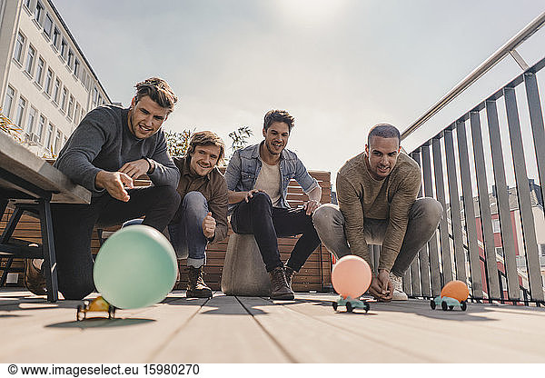 Group of friends making a toy car race with balloons on a balcony