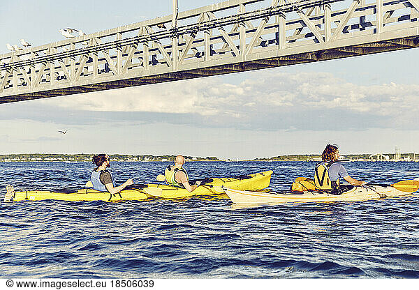 Group of kayakers paddle under a bridge at sunset in Casco Bay  Maine