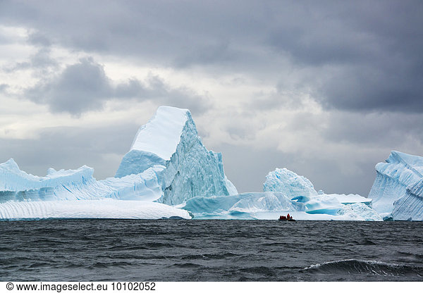 Group of people crossing the ocean in the Antarctic in a rubber boat  icebergs in the background.
