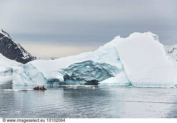 Group of people crossing the ocean in the Antarctic in a rubber boat  icebergs in the background.