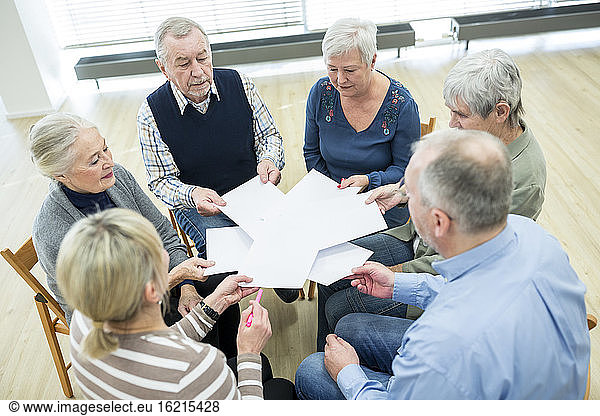 Group of seniors attending therapy group in retirement home  using sheets of paper