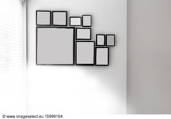 Group of various blank black picture frames on grey wall near a window with light space for text closeup.
