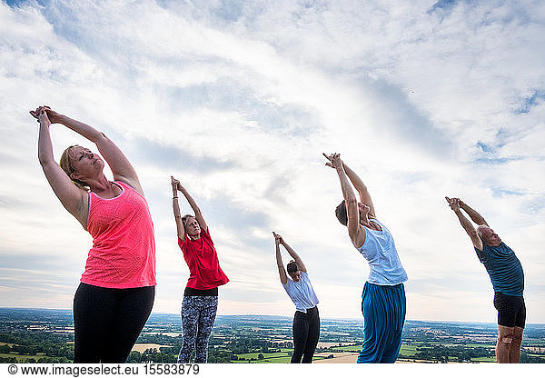 Group of women and men taking part in a yoga class on a hillside.