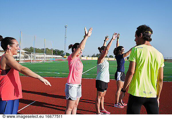 group of women practice pre-workout stretching with their young traine