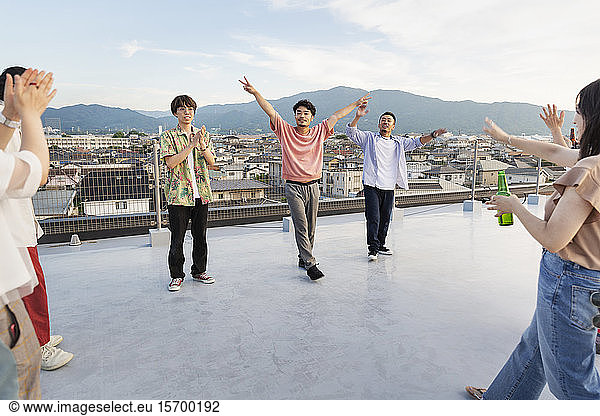 Group of young Japanese men and women dancing on a rooftop in an urban setting.