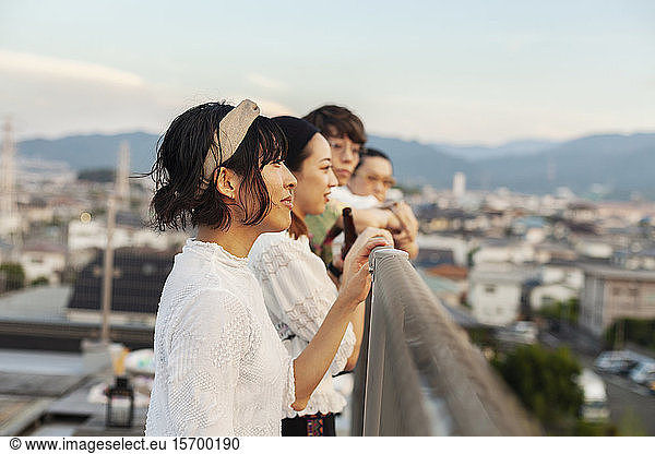 Group of young Japanese men and women standing on a rooftop in an urban setting.