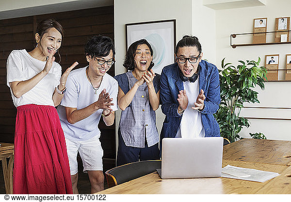 Group of young Japanese professionals looking at laptop computer in a co-working space  smiling and cheering.