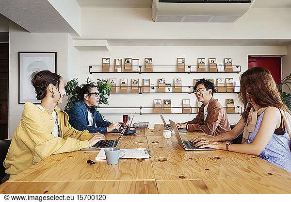 Group of young Japanese professionals working on laptop computers in a co-working space.