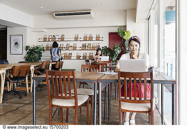 Group of young Japanese professionals working on laptop computers in a co-working space.